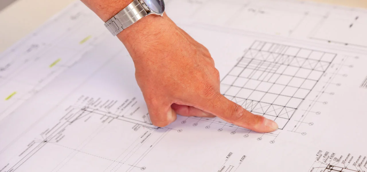Hand mit Armbanduhr zeigt auf Konstruktionsplan  INT-BAU
